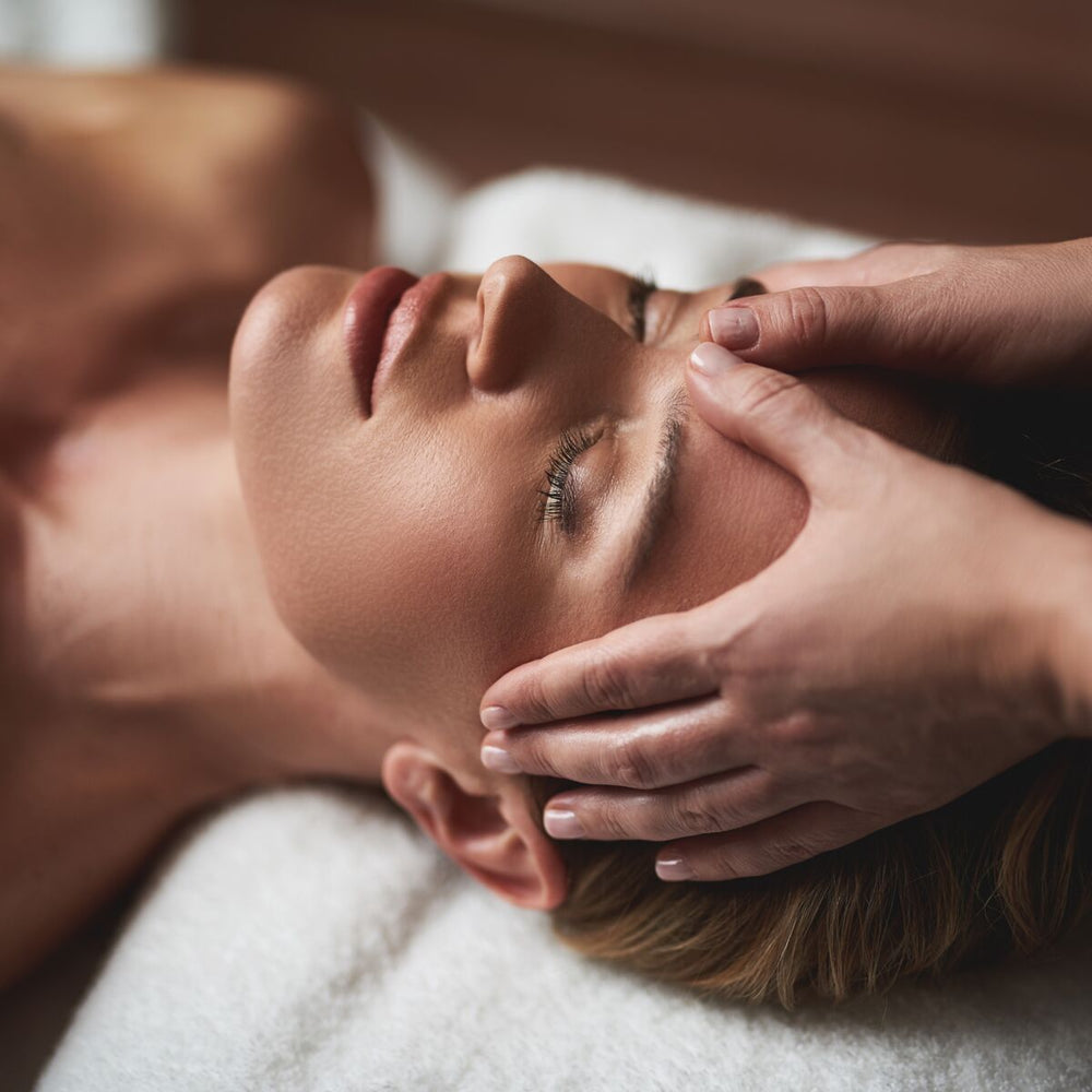 Massage du visage : des mains posées sur les tempes d'une femme détendue